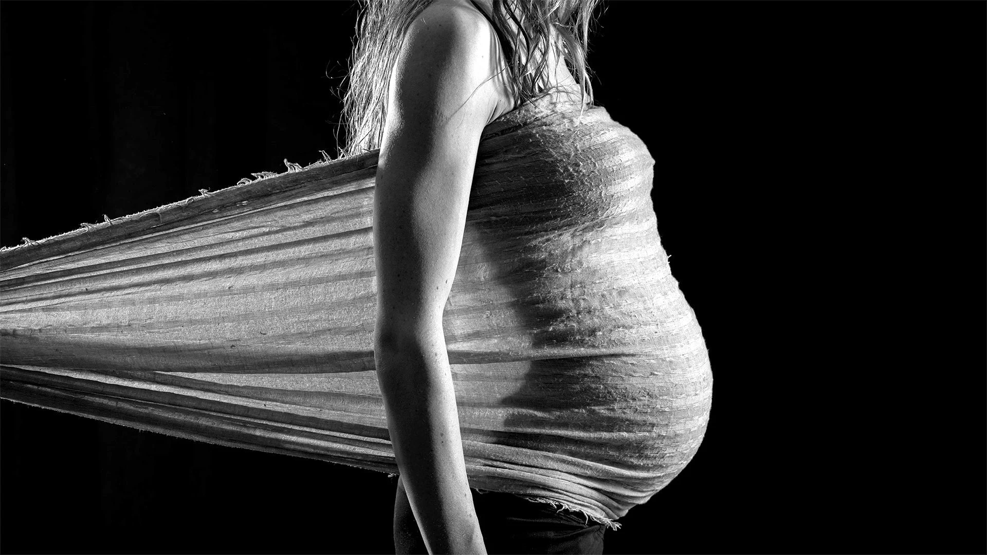 Future maman de profil, ventre rond enveloppé d'un voile en mouvement — séance grossesse en noir et blanc