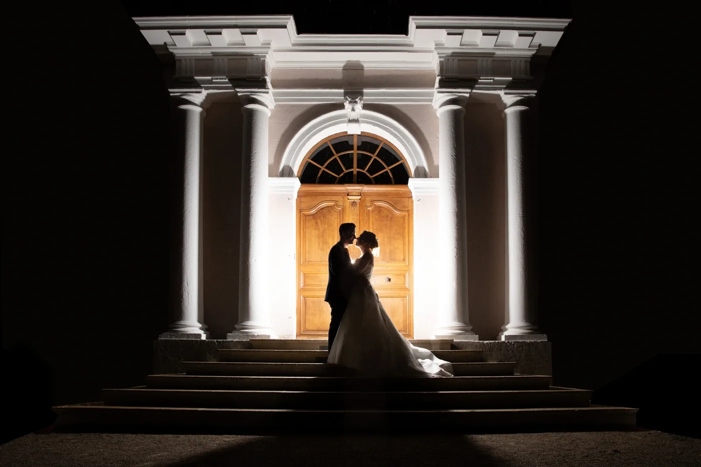 Silhouettes des mariés devant une porte éclairée la nuit — photo de mariage créative