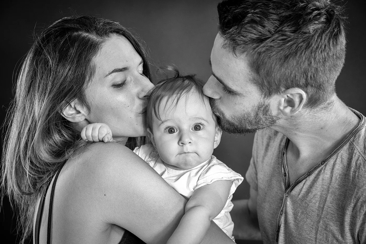 Portrait de famille en noir et blanc : les parents embrassent leur bébé — séance naissance au studio Partenaire Image
