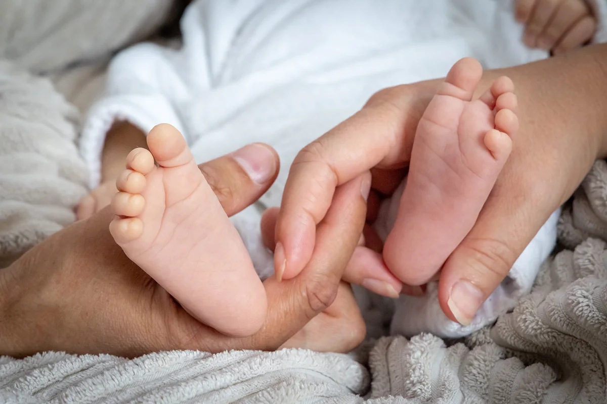 Petits pieds de nouveau-né dans les mains de sa maman — séance naissance
