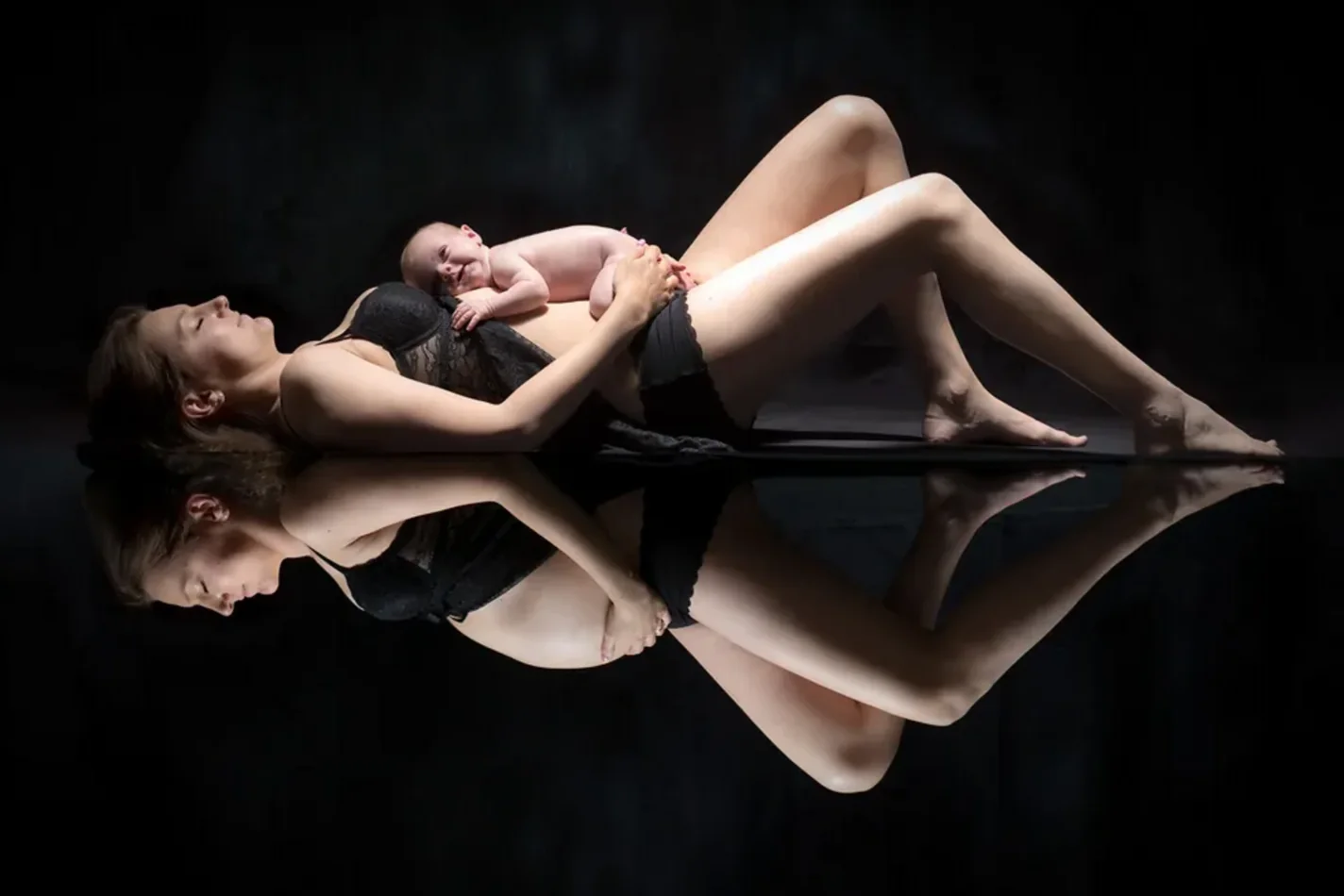 Nouveau-né endormi sur sa maman, effet miroir sur fond noir — séance nouveau-né au studio Partenaire Image